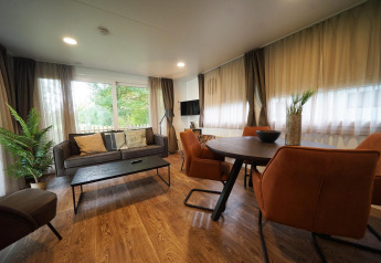 Modern ingerichte lodge woonkamer met grote ramen, ronde eettafel en comfortabele bruine stoelen.