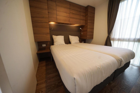 Modern bedroom at Cottage at Kaatsheuvel, Netherlands, with twin beds, wood cabinets, and large window.