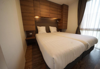 Modern bedroom at Cottage at Kaatsheuvel, Netherlands, with twin beds, wood cabinets, and large window.