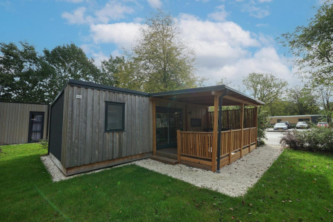 Træhytte med overdækket terrasse og haveområde ved Cottage at Kaatsheuvel, Holland, på en solrig dag.