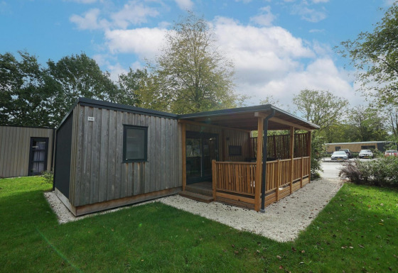 Træhytte med overdækket terrasse og haveområde ved Cottage at Kaatsheuvel, Holland, på en solrig dag.