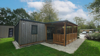 Træhytte med overdækket terrasse og haveområde ved Cottage at Kaatsheuvel, Holland, på en solrig dag.