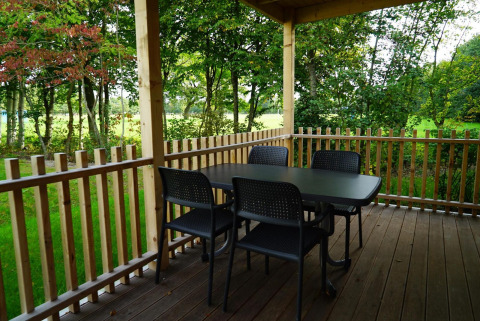 En overdækket terrasse med bord og fire stole på Cottage at Kaatsheuvel, omgivet af grønne træer.