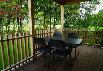 En overdækket terrasse med bord og fire stole på Cottage at Kaatsheuvel, omgivet af grønne træer.