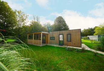 Moderne trælodge kaldet Cottage ved Kaatsheuvel i Holland, omgivet af grønne træer og en græsplæne.