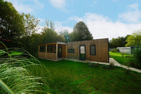 Casa de madera moderna llamada Cottage at Kaatsheuvel en Países Bajos, rodeada de césped y árboles verdes.