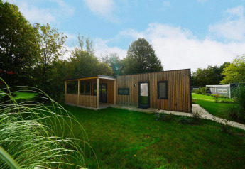 Moderne houten lodge genaamd Cottage bij Kaatsheuvel, Nederland, omgeven door gras en bomen.