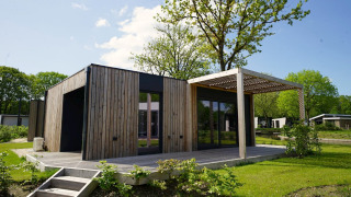 Modern Domus lodge with wood paneling, a patio, and lush greenery under a bright blue sky.