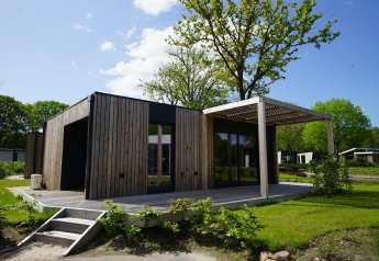 Hedendaagse Domus-lodge met houten bekleding, terras en tuin, te midden van groene omgeving.