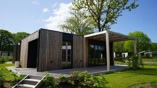 Lodge Domus moderna con paneles de madera, terraza y vegetación, rodeada de árboles y cielo claro.