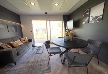 Modernes Wohnzimmer in der Domus Lodge, Kaatsheuvel, Niederlande mit Esstisch, Sofa und Gartenausblick.
