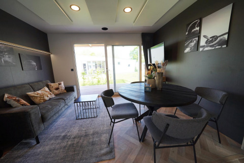 Modern lounge at Domus lodge in Kaatsheuvel, Netherlands, with dining table, sofa and garden view.
