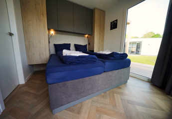 Modernes Schlafzimmer in der Domus-Lodge in Kaatsheuvel, Niederlande, mit blauer Bettwäsche und Gartenblick.