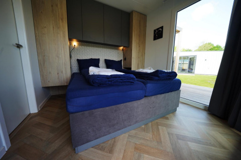 Modern bedroom at Domus lodge in Kaatsheuvel, Netherlands, with blue bedding and large window to the garden.