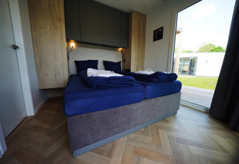 Dormitorio moderno en el lodge Domus en Kaatsheuvel, Países Bajos, con ropa de cama azul y gran ventana al jardín.