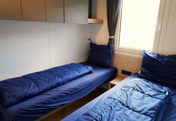 Zwei Einzelbetten mit blauer Bettwäsche in der Domus Lodge in Kaatsheuvel, Niederlande, bei Fenster.