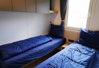 Twee eenpersoonsbedden met blauwe lakens in Domus Lodge in Kaatsheuvel, Nederland, bij het raam.