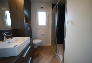 Baño moderno en la cabaña Domus, Kaatsheuvel, Países Bajos, con ducha, inodoro y lavabo minimalista.