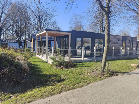 Modern Domus lodge at Kaatsheuvel in the Netherlands, featuring a wooden terrace, large windows and greenery.