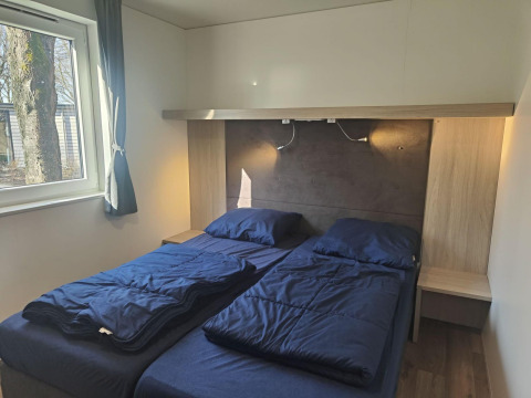 Habitación con dos camas individuales, ropa de cama azul y ventana, tomada en Domus lodge en Kaatsheuvel, Países Bajos.