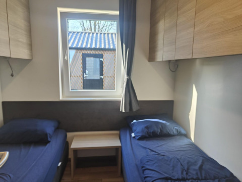 Room at Domus lodge in Kaatsheuvel, Netherlands, with twin beds, storage cabinets, and outside view.