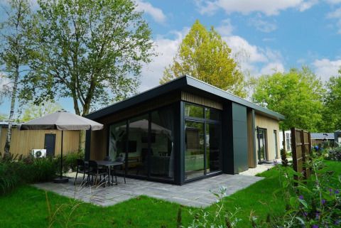 Lodge moderno Pavilion Maximaal con fachada de cristal y terraza con sombrilla, rodeado de naturaleza verde.