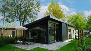 Moderne lodge bij Pavilion Maximaal met terras, glazen zijgevel en groene tuin met bomen en planten.
