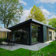 Moderne lodge ved Pavilion Maximaal omgivet af grønne træer, terrasse med parasol og udendørs siddeområde.