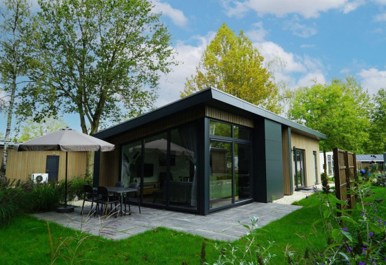 Moderne lodge Pavilion Maximaal met glazen gevel, terras, parasol en omringd door groene natuur en bomen.