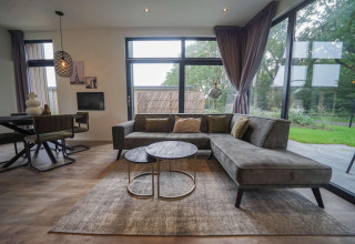 Modern living room at Pavilion Maximaal lodge in Kaatsheuvel, Netherlands, with large windows and greenery.