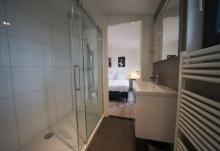 Salle de bain moderne avec douche en verre et lavabo, ouverte sur une chambre au Pavilion Maximaal, Kaatsheuvel.