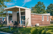 Modern Tiny Cottage lodge in Kaatsheuvel, Netherlands, surrounded by lush green garden and trees.