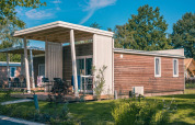 Moderne lodge kaldet Tiny Cottage i Kaatsheuvel, Holland, omgivet af grønne træer og haver.
