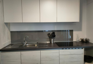 Modern kitchenette at Tiny Cottage in Kaatsheuvel, Netherlands, featuring white cabinets and black countertop.