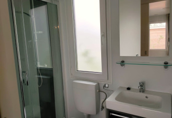 Badkamer in Tiny Cottage Kaatsheuvel met douche, toilet, wastafel, raam en spiegel met glazen plank.