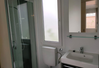 Baño en Tiny Cottage Kaatsheuvel con ducha, inodoro, lavabo, ventana y espejo sobre estante de vidrio.