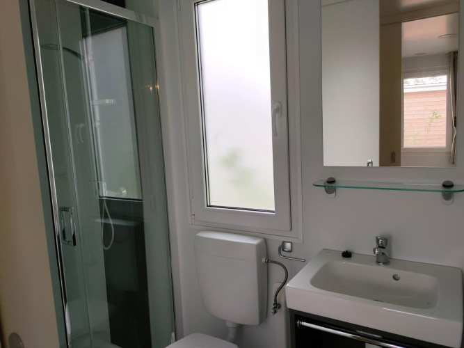 Badezimmer im Tiny Cottage Kaatsheuvel mit Dusche, WC und Waschbecken neben Fenster und Spiegel.