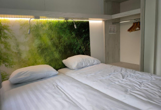 Habitación moderna con cama doble, sábanas blancas y mural naturalista en Tiny Cottage en Kaatsheuvel.