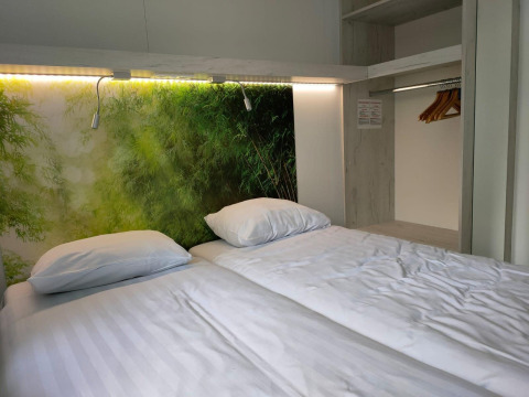 Chambre moderne avec grand lit, draps blancs, fresque nature et placard ouvert au Tiny Cottage, Kaatsheuvel.