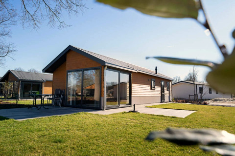 Velthorst-Lodge mit moderner Holzfassade und großen Fenstern, umgeben von grünem Rasen bei Sonne.