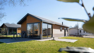 Lodge Velthorst moderno con exterior de madera, grandes ventanales y terraza en un césped soleado.