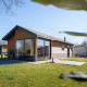 Moderne Velthorst-lodge met houten buitenkant, grote ramen en terras op een zonnig groen grasveld.