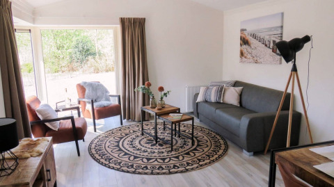 Bright lounge area in a lodge with modern furnishings, large windows, grey sofa, and stylish décor.