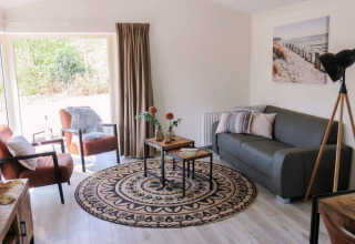 Bright lounge area in a lodge with modern furnishings, large windows, grey sofa, and stylish décor.