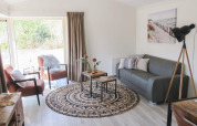Sala luminosa en una cabaña con mobiliario moderno, grandes ventanales, sofá gris y decoración chic.