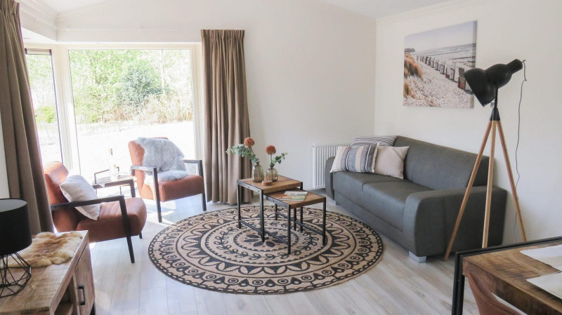 Sala luminosa en una cabaña con mobiliario moderno, grandes ventanales, sofá gris y decoración chic.