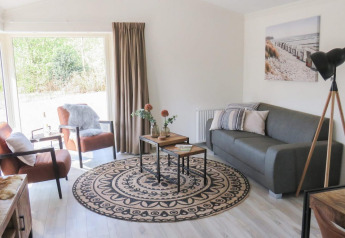 Lichte woonkamer in een lodge met moderne meubels, grote ramen, grijze bank en stijlvolle uitstraling.