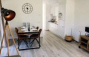 Intérieur lumineux de lodge avec coin repas, cuisine moderne, lampadaire et grande horloge murale.