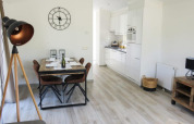 Interior de lodge luminoso con comedor, cocina moderna, lámpara de pie y reloj decorativo de pared.