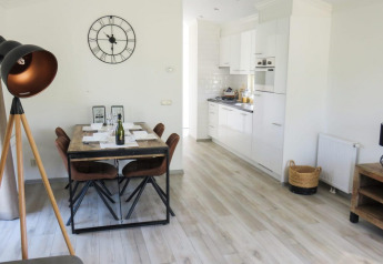 Licht lodge-interieur met een eetruimte, moderne keuken, vloerlamp en grote wandklok.